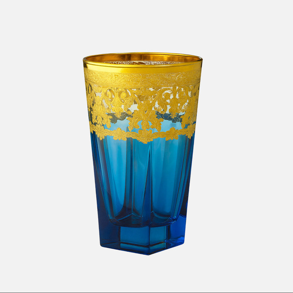 A blue and gold decorative drinking glass with a faceted geometric design, featuring a wide gold band with an intricate cutout pattern around the upper half, set against a plain light gray background.